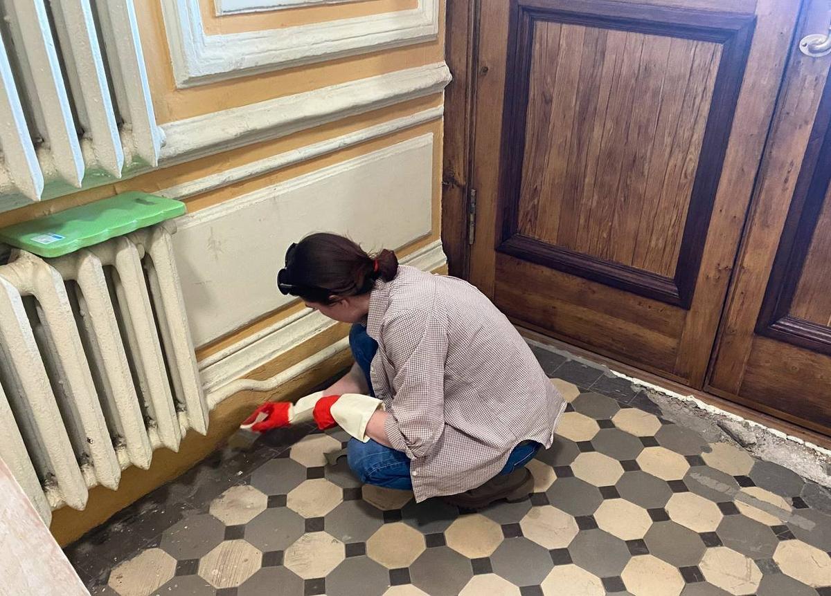 Волонтёр чистит плитку в доме Романова. Фото: фонд «Внимание»